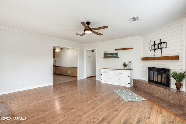 unfurnished living room with ceiling fan, a large fireplace, crown molding, and hardwood / wood-style flooring