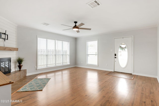 foyer entrance featuring ceiling fan, a tiled fireplace, crown molding, and hardwood / wood-style floors