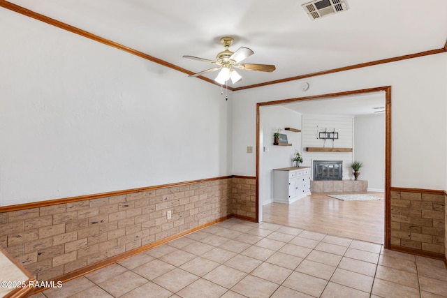 empty room with ceiling fan, light tile patterned floors, a fireplace, and ornamental molding