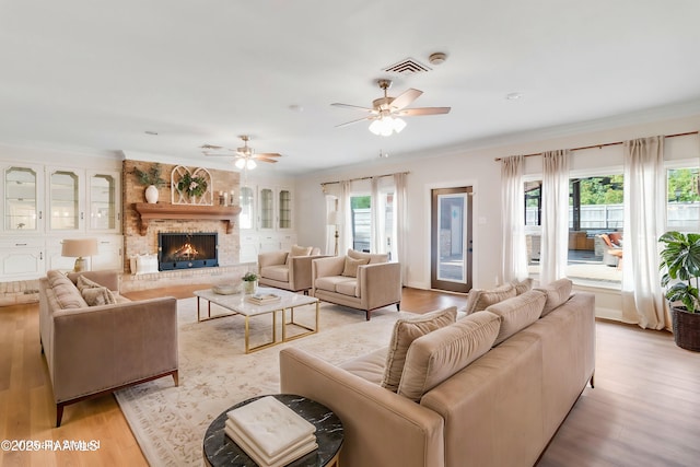 living room with crown molding, a brick fireplace, ceiling fan, and light hardwood / wood-style flooring