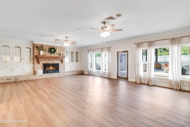 unfurnished living room with ornamental molding, ceiling fan, light wood-type flooring, and a fireplace