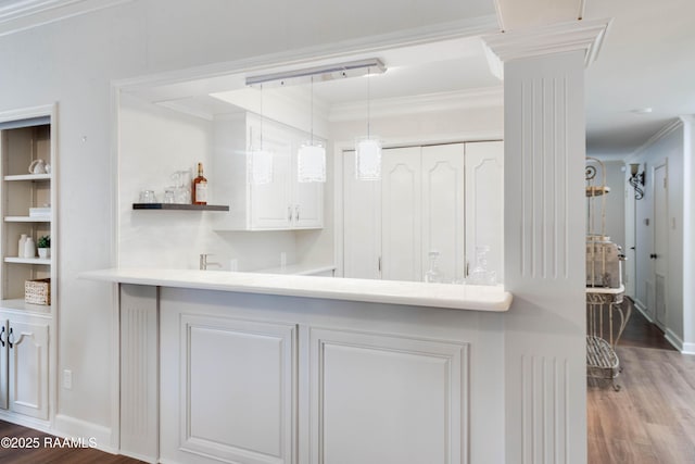 kitchen featuring kitchen peninsula, hanging light fixtures, hardwood / wood-style floors, crown molding, and white cabinetry