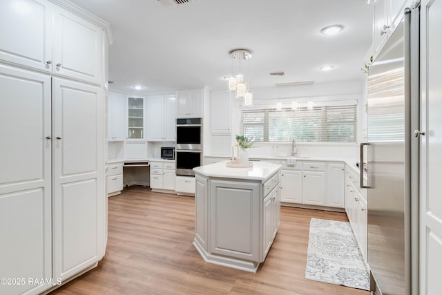 kitchen with white cabinetry, appliances with stainless steel finishes, a kitchen island, light hardwood / wood-style flooring, and decorative light fixtures