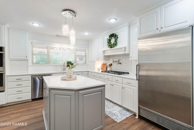 kitchen featuring appliances with stainless steel finishes, a kitchen island, decorative backsplash, white cabinetry, and decorative light fixtures