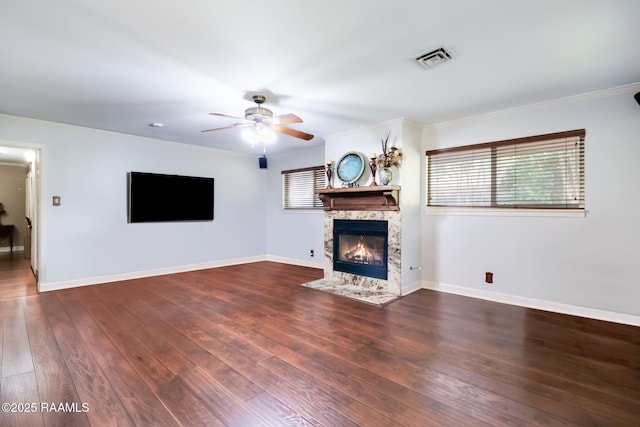 unfurnished living room with ceiling fan, a premium fireplace, crown molding, and dark wood-type flooring