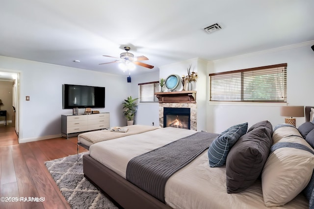 bedroom featuring a premium fireplace, ceiling fan, hardwood / wood-style flooring, and ornamental molding