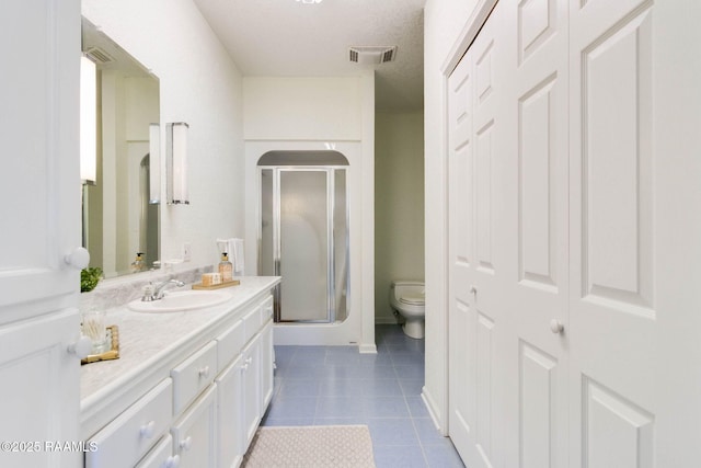 bathroom with a shower with shower door, vanity, tile patterned flooring, and toilet