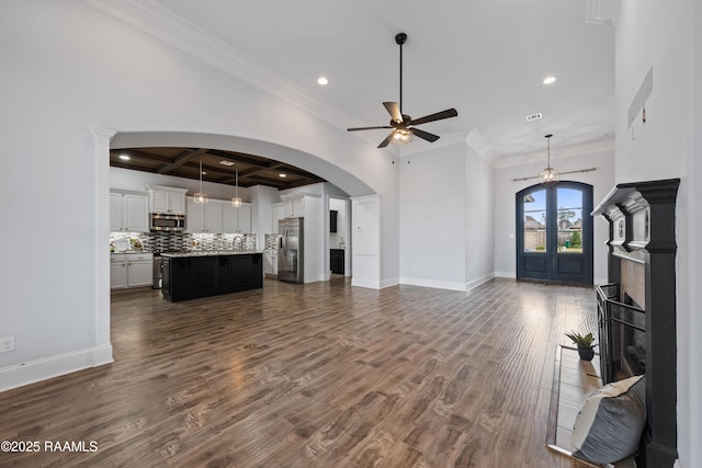 unfurnished living room featuring ceiling fan, dark hardwood / wood-style floors, beam ceiling, ornamental molding, and french doors