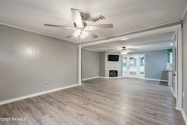 unfurnished living room featuring ceiling fan, ornamental molding, a textured ceiling, and light wood-type flooring