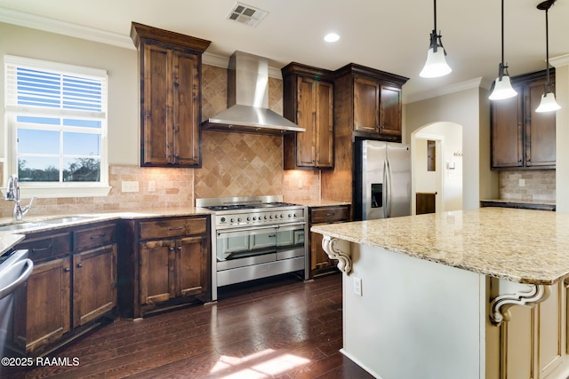 kitchen with appliances with stainless steel finishes, sink, hanging light fixtures, light stone countertops, and wall chimney exhaust hood