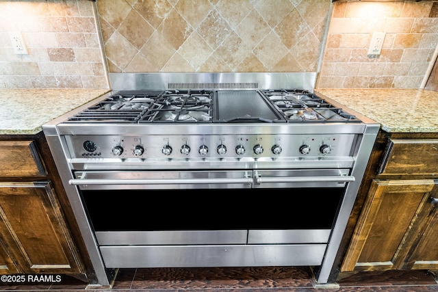 kitchen with light stone counters, dark brown cabinetry, double oven range, and backsplash