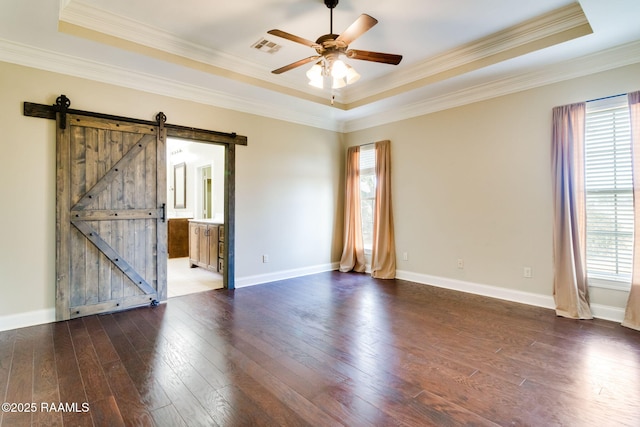 empty room featuring a raised ceiling, a barn door, dark wood-type flooring, and ceiling fan