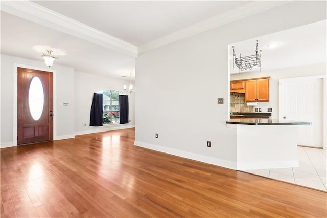 entrance foyer featuring ornamental molding, baseboards, light wood finished floors, and an inviting chandelier