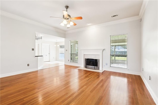 unfurnished living room featuring light wood-style flooring, ceiling fan with notable chandelier, visible vents, a tiled fireplace, and crown molding