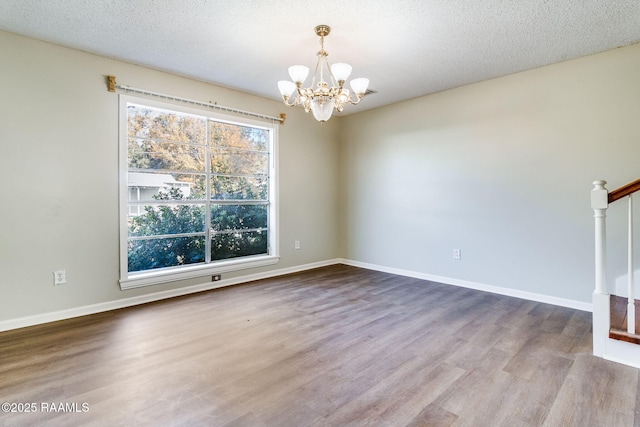 empty room featuring hardwood / wood-style flooring, a textured ceiling, and an inviting chandelier