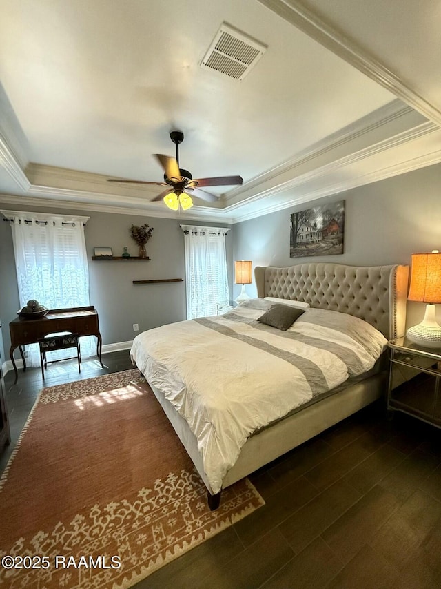 bedroom with dark wood-type flooring, ornamental molding, a raised ceiling, and ceiling fan