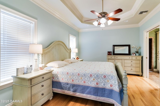 bedroom with crown molding, a tray ceiling, light hardwood / wood-style floors, and ceiling fan