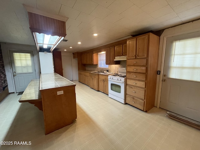 kitchen featuring white range with gas stovetop, a wealth of natural light, and tile countertops