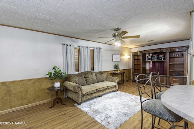 living room featuring ceiling fan, wooden walls, ornamental molding, and light hardwood / wood-style floors