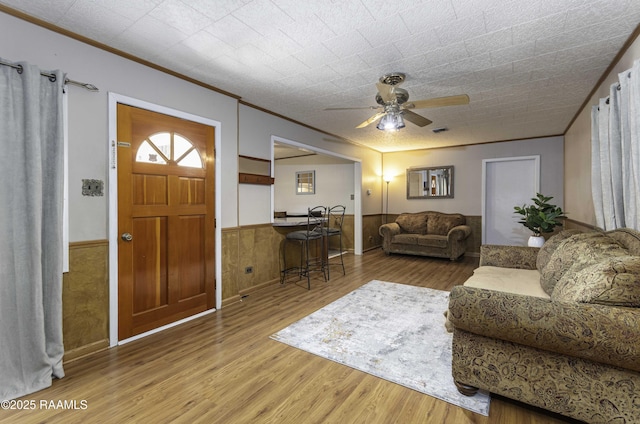 living room with ceiling fan, wood-type flooring, wood walls, and crown molding