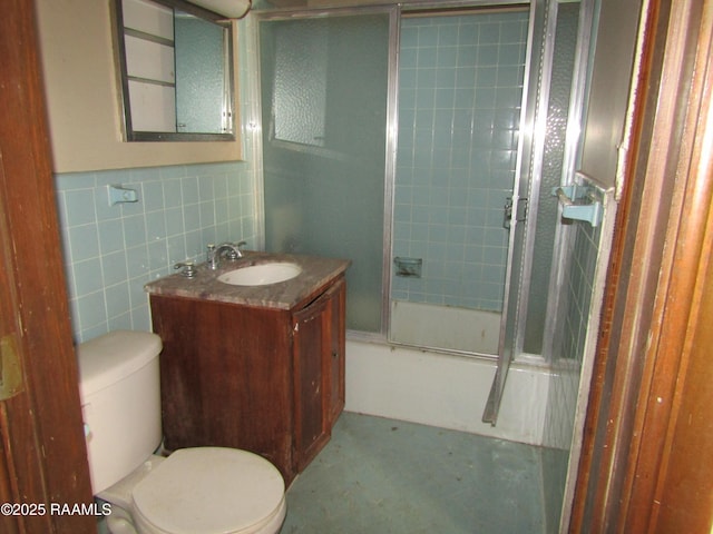 full bathroom featuring combined bath / shower with glass door, vanity, tile walls, and toilet