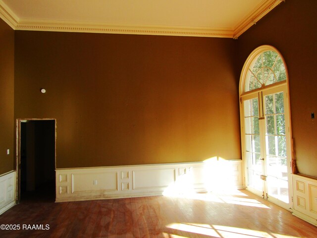 empty room with crown molding, a wainscoted wall, a decorative wall, and wood finished floors