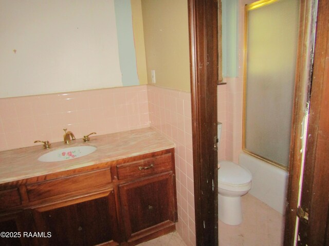 bathroom featuring tile walls, a wainscoted wall, vanity, toilet, and enclosed tub / shower combo