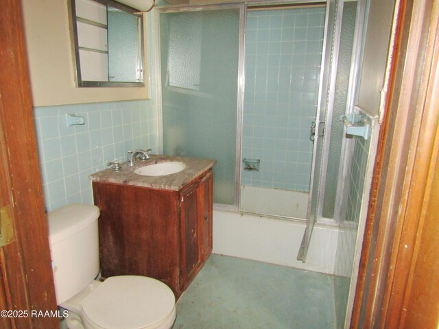 full bath with toilet, tile walls, shower / bath combination with glass door, and vanity