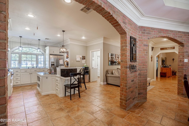 kitchen with arched walkways, hanging light fixtures, a kitchen island with sink, a kitchen bar, and stainless steel refrigerator with ice dispenser