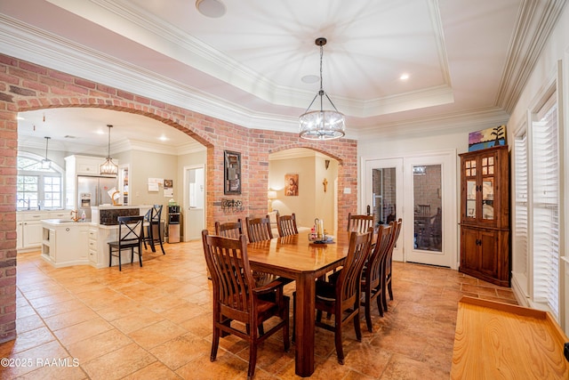 dining space with arched walkways, a tray ceiling, french doors, and brick wall