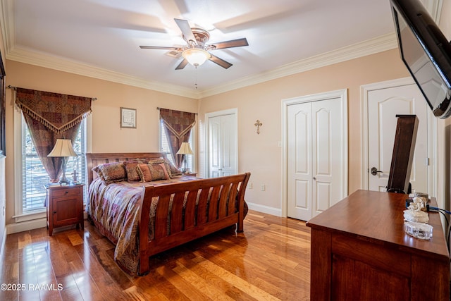 bedroom featuring light wood-style floors, ornamental molding, baseboards, and two closets