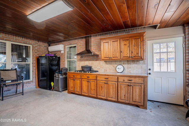 kitchen with an AC wall unit, wall chimney range hood, light countertops, freestanding refrigerator, and stainless steel gas stovetop