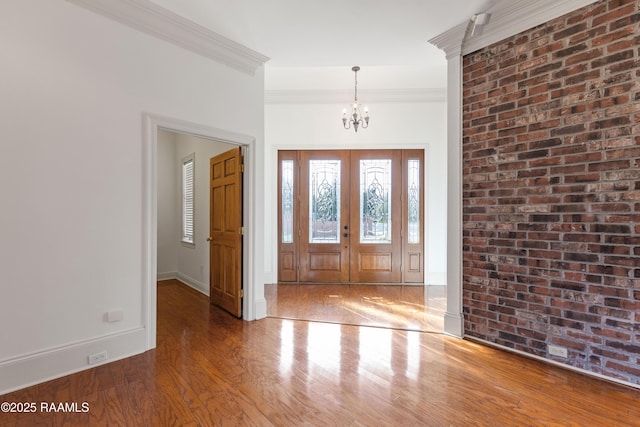 foyer entrance with an inviting chandelier, hardwood / wood-style floors, ornamental molding, brick wall, and french doors