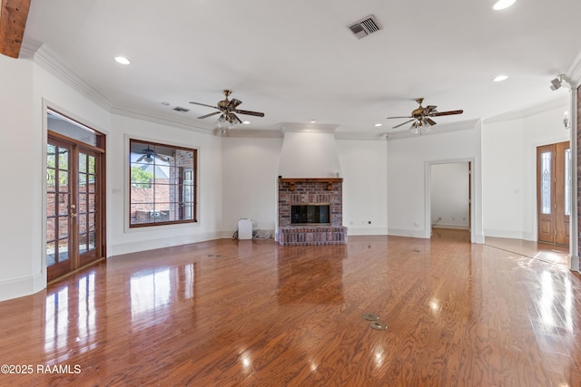 unfurnished living room with a brick fireplace, crown molding, french doors, and light wood-type flooring