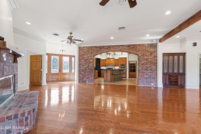 unfurnished living room featuring light hardwood / wood-style flooring, ceiling fan, ornamental molding, a brick fireplace, and beamed ceiling