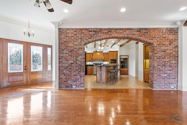 unfurnished living room with crown molding, brick wall, ceiling fan with notable chandelier, and light wood-type flooring