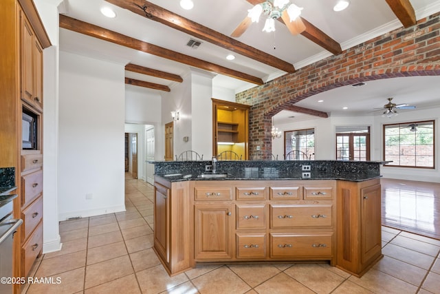 kitchen featuring brick wall, sink, dark stone counters, light tile patterned floors, and beam ceiling