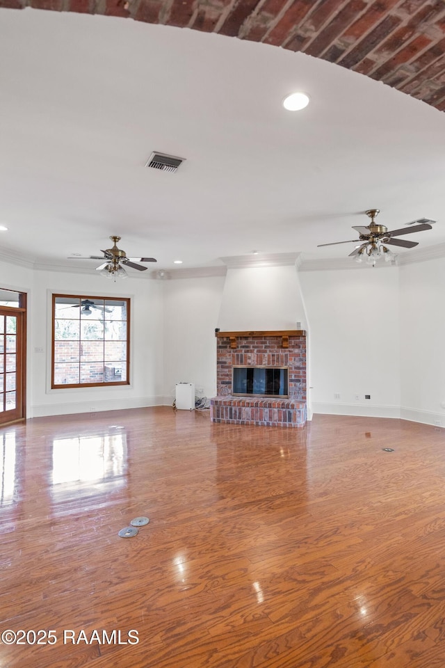 unfurnished living room featuring a brick fireplace, ornamental molding, hardwood / wood-style floors, and ceiling fan