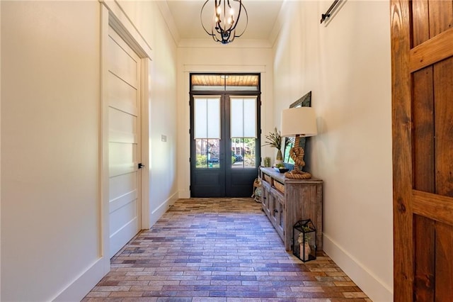 foyer featuring brick floor, crown molding, baseboards, and an inviting chandelier