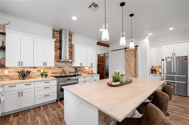 kitchen with crown molding, visible vents, a barn door, appliances with stainless steel finishes, and wall chimney range hood