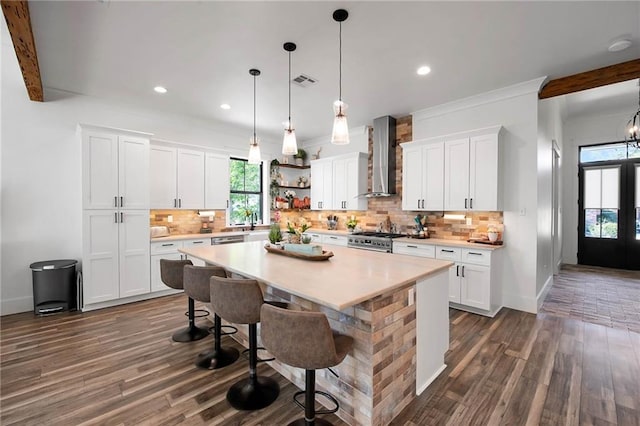 kitchen featuring stainless steel stove, light countertops, wall chimney range hood, and open shelves