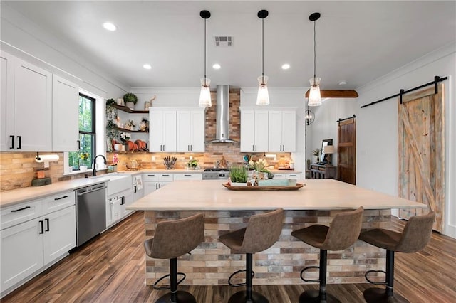 kitchen featuring a barn door, visible vents, dishwasher, wall chimney exhaust hood, and a sink