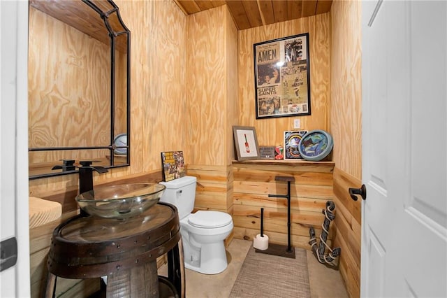 half bath with wood ceiling, wood walls, a sink, and toilet