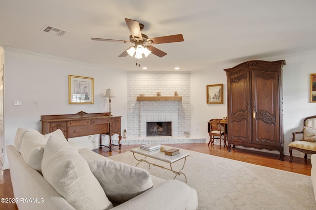 living room with a brick fireplace, crown molding, light hardwood / wood-style flooring, and ceiling fan