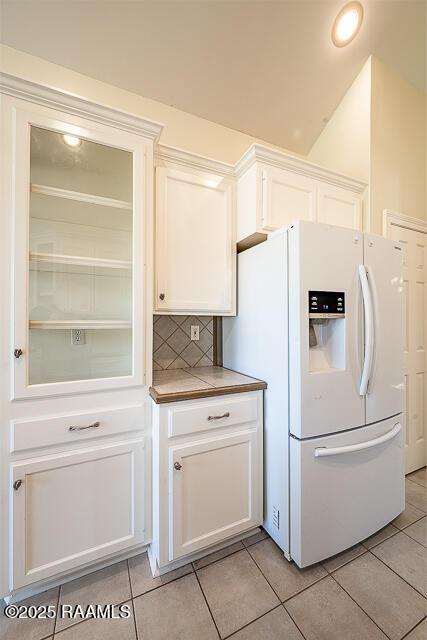 kitchen with light tile patterned floors, backsplash, white fridge with ice dispenser, and white cabinets