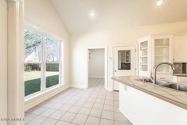 kitchen featuring tile counters, light tile patterned floors, sink, backsplash, and vaulted ceiling