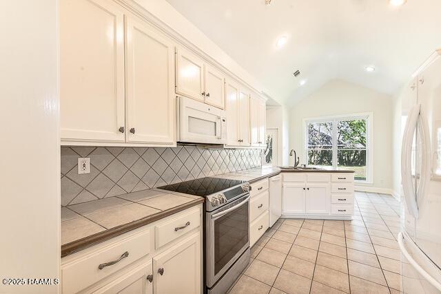 kitchen featuring white appliances, tile counters, white cabinetry, sink, and vaulted ceiling