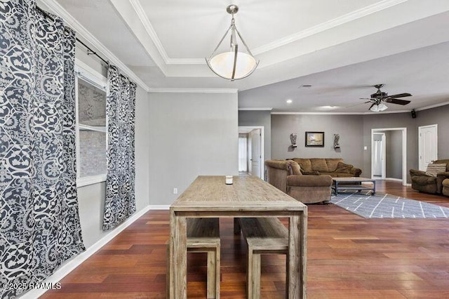 dining space featuring dark wood-type flooring, ceiling fan, ornamental molding, and a raised ceiling