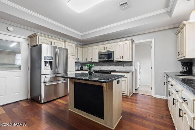 kitchen with cream cabinetry, stainless steel appliances, dark stone counters, and a center island