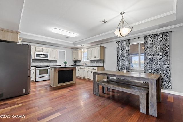 kitchen with sink, decorative light fixtures, a tray ceiling, stainless steel appliances, and cream cabinets